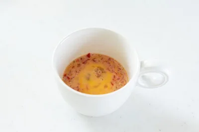 作り方２：耐熱マグカップに卵を割り入れ、粗みじん切りのミニトマトを加えて混ぜる。