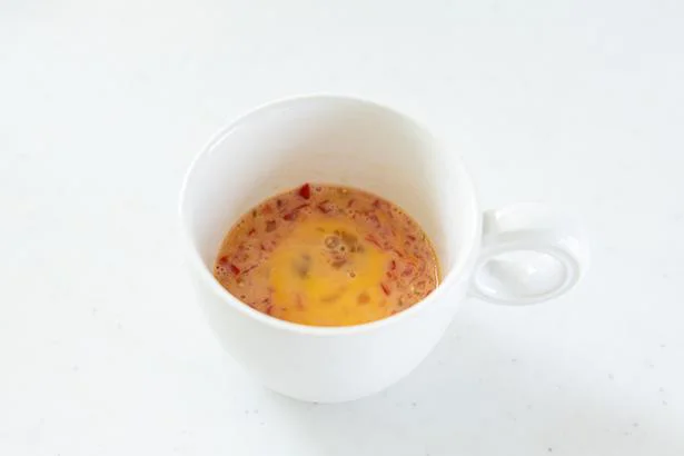 作り方２：耐熱マグカップに卵を割り入れ、粗みじん切りのミニトマトを加えて混ぜる。