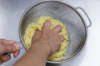 ゆで上がった乾麺は、手でもむようによく洗ってぬめりを取り、ざるにぎゅーっと押し付けてしっかり水気を切ります