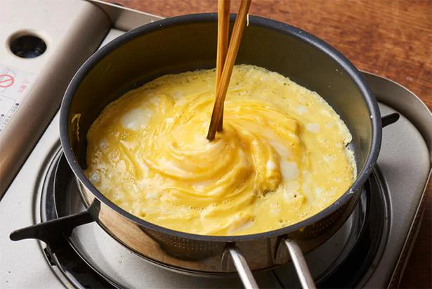 卵の両端から菜箸を入れ込み、中央に寄せ、菜箸を固定したまま、フライパンを時計回りに回す