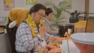忙しい年末に焼きいもをほおばりながら仕事をこなす露の先輩、保ケ辺さん