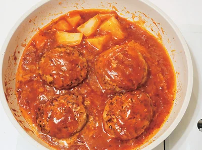【作り方4】ソースの材料とじゃがいも、にんじんを入れ、蓋をして弱火で10分煮込む。最後にバターを入れる。トマト、レタスと盛りつけ、トッピングをする。