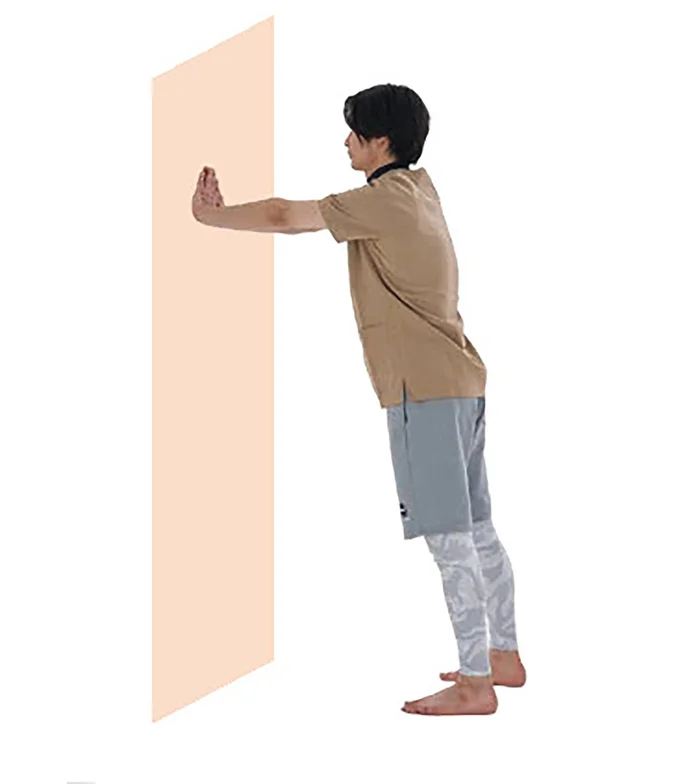 1. 肩の高さで腕をまっすぐに伸ばし、壁に手をつく。