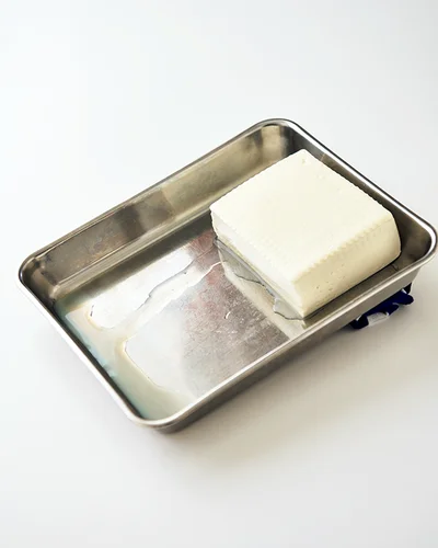 豆腐をバットの端にのせ、高さ２〜３cmの高低差をつけて斜めに置く。そのまま15〜20分おき、たまった水を捨てるだけ。縁のある皿でもOK！