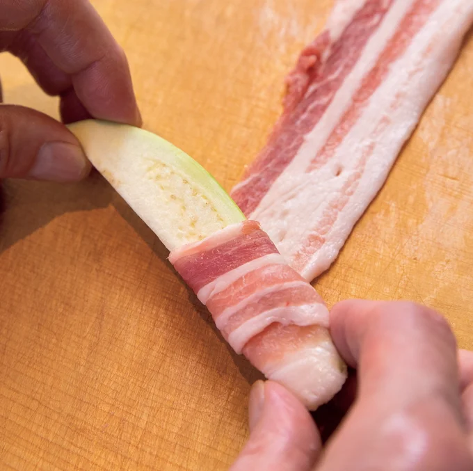 なすをやや斜めに置いて転がしながら、豚肉をくるくるとすき間なく巻きつけます