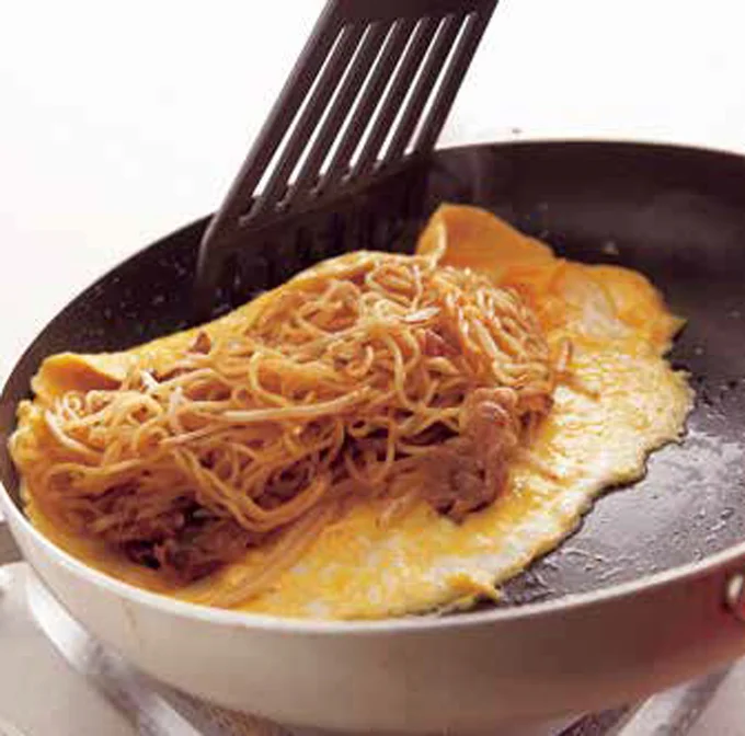 卵の上に焼きそばをのせたらフライパンの縁に寄せ、フライ返しで卵の手前と奥を返して包む。