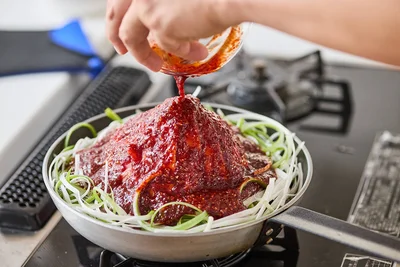 玉ねぎ、豆もやしを豚肉で覆い、周りに長ねぎをのせ、全体にAをかける