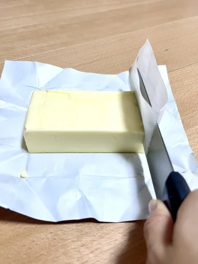 クッキングシートを挟んだ包丁で、使いたいサイズにバターをカット（▶︎次へ）