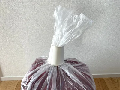 圧縮したい服を入れたビニール袋の口に紙コップを通す（▶次へ）