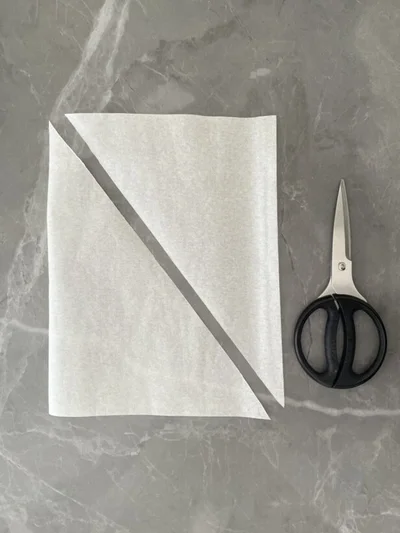 三角形が2枚できるよう、クッキングシートを斜めにカット（▶次へ）