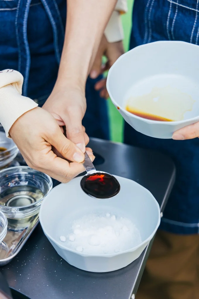 小山さんの持つ計量スプーンをボウルに傾けるみきさん