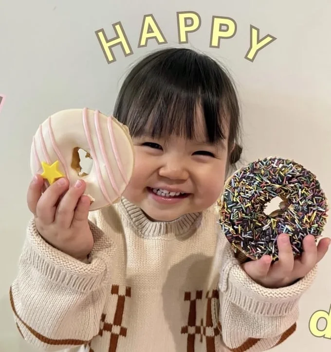ドーナツ両手にスマイル▶ （次画像から兄は妹を溺愛し、妹も兄が大好き！ ほのぼの育児コミックエッセイ『しおさん1歳 令和ギャル爆誕の道のり』が読めます）