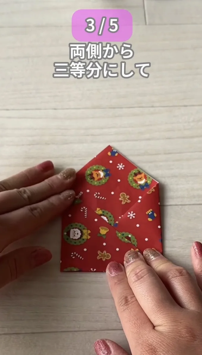 左右の角を内側へ折り込む▶上の角の手前1枚を折り下げ…（⇒次へ）