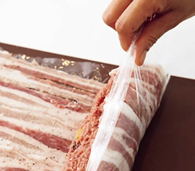 豚薄切り肉を並べた上に肉だねを置き、ラップを持ち上げて手前からくるくると巻く。