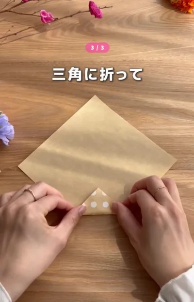 折り紙の下の角を小さい三角に折る▶続いて左右を折り…（⇒次へ）
