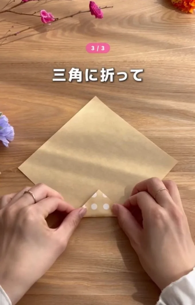 折り紙の下の角を小さい三角に折る▶続いて左右を折り…（⇒次へ）