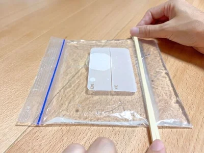 水の入ったジップ付き保存袋を割りばしで挟む（▶次へ） 