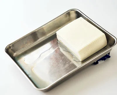 豆腐をバット（または縁のある皿）の端に寄せ、高さ2～3cmの高低差をつけて斜めに置く