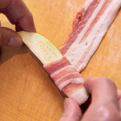 なすをやや斜めに置いて転がしながら、豚肉をくるくるとすき間なく巻きつけます