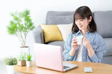 コップを持ってパソコンに向かう女性の画像