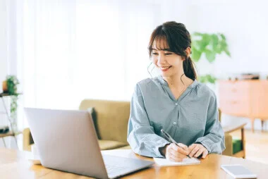 女性がメモを取りながらPCに向かっている画像