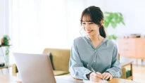 女性がメモを取りながらPCに向かっている画像