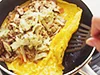 半熟状に広げて焼いた、卵の向こう半分に具をのせ、手前半分を上からかぶせるようにして包む。
