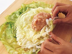大きめの葉を少しずらして重ね、まん中に残りのキャベツを葉の大きい順に重ねる。ひき肉だねをのせたら、手前からしっかりと包む。