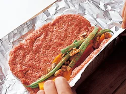 ひき肉だねはアルミホイルより一回り小さくなるようにのばす。手前から太巻きずしを作るように巻いていく。