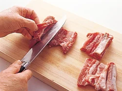 スペアリブは、まず骨に沿って切り目を入れて開き、さらに肉の厚みを半分に開く。これを半分に切って２枚に。