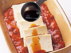味がなじみやすいように、ミートソースで豆腐をサンドするように耐熱容器に入れる。しょうゆは豆腐に直接かけるとよい。