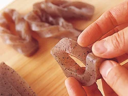 薄切りにしたこんにゃくに切り目を入れ、切れ目に片端を通すと見た目も華やかに、味もしみこみやすい。