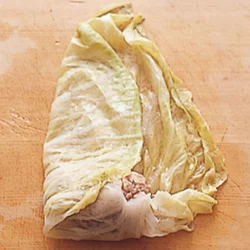 たねをキャベツの手前にのせて一度巻き、片側の葉を内側に折る。