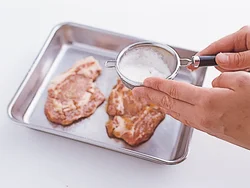 汁を軽くきった豚肉は、茶こしで小麦粉を薄くふる。焼いたときに表面を固めてうまみを閉じ込めてくれる。