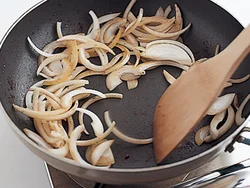 肉を焼いたあとのフライパンについた肉のうまみを、木べらでこそげて玉ねぎを炒める。