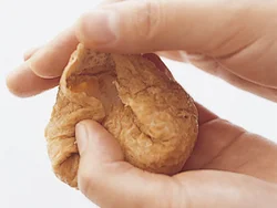 両手のひらではさむように汁けを絞る。油揚げにすし飯を詰め、中で軽く広げる。油揚げの端を中に折り、余った両端を折りたたむ。