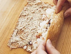 油揚げを開いて広げ、すし飯を棒状にまとめて手前に置く。くるくると巻きずしのように巻いて、食べやすく切る。