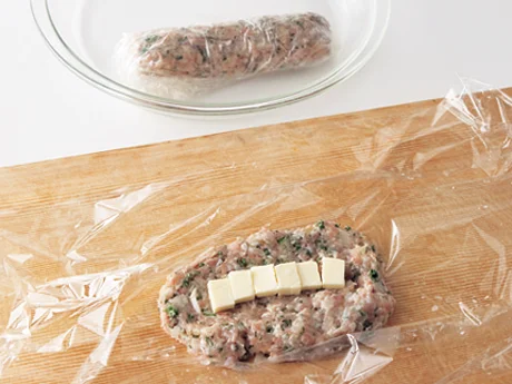 ラップの上にひき肉だねを広げ、チーズを置いて棒状に形を整える。肉汁が出るので耐熱皿に入れて加熱する。