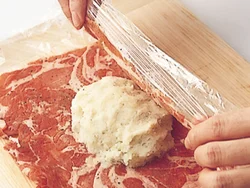 つぶしたじゃがいものまん中にチーズを入れ、広げた豚肉をラップごと持ち上げて包む。