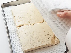 ペーパータオルに豆腐を包み、そのままおいて水きり。豆腐の水分もうまみになるので、味つけがうすまらないように程よく水をきることが目的。豆腐を切ってからペーパーに包むと、より短時間で水きりできる。