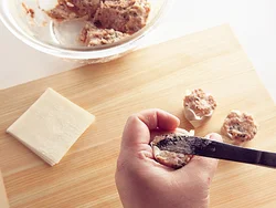 ひき肉だねをのせた皮を、親指と中指で輪を作って持ち、表面をナイフでならしながら形を整える。