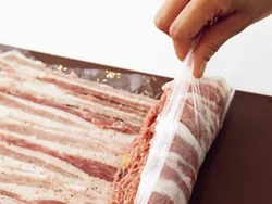 豚薄切り肉を並べた上に肉だねを置き、ラップを持ち上げて手前からくるくると巻く。