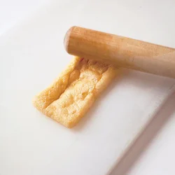 油揚げは煮る前に、すりこ木で表面を軽くたたいておく。こうすると中の繊維がほぐれ、袋状に開きやすくなる。