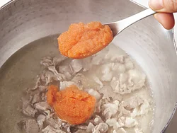 豚肉の色が変わったら、薄皮を除いた明太子を大きめのスプーンで加え、手早くほぐしながら混ぜる。豆腐は手でくずして加えて。