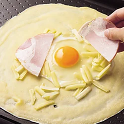 生地を広げたそばから具をのせて一緒に焼く。卵は滑りやすいので、ゆっくりと割り入れて。