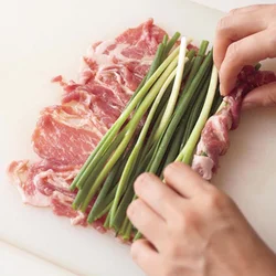 万能ねぎの長さに合わせて豚肉を広げ、ねぎを上にのせる。くるくるときつめに巻きつけると、きれいなうず巻き状に仕上がる。