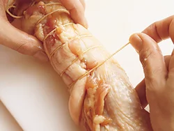 丸めたとり肉をたこ糸で巻く。たこ糸は、一方の端で１周させてからしっかり結び、全体にくるくると巻く。さらに巻き終わりもしっかり結び、ほどけないようにする。