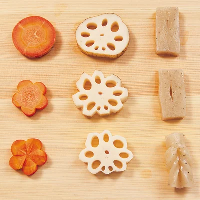 飾り切りで華やかさアップ!
●ねじり梅
1.にんじんは皮をむいて7〜8mm厚さの輪切りにし、梅の抜き型で抜く。
2.中心から花びらと花びらの間に向かって厚みの半分くらいまで切り目を入れる。
3.花びらのまん中から切れ目に対して斜めに包丁を入れ、そぎ取る。
●花れんこん
1.れんこんは皮つきのまま7〜8mm厚さの輪切りにする。
2.れんこんの周囲の穴と穴の間の部分を直角に少し切り落とす(抜き型の角の部分を使うとラク)。
3.残ったれんこんの皮を包丁でそぎ取るようにして、円い花びらの形にする。
●手綱こんにゃく
1.こんにゃくは4cm長さ、1.5cm幅、7〜8mm厚さに切る。
2.まん中に1本、上下を切り離さないように切り目を入れる。
3.一方の端を切れ目にくぐらせて、引き出す。
※はちみつが入っているので、1歳未満のお子さんには食べさせないでください。