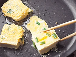 スプーンで卵液ごと豆腐をすくい、卵液をのばしながらフライパンに入れる。豆腐をのばした卵側に返して、全体を卵で包む。