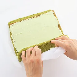 手前のペーパーごと持ち上げ、生地を指で押さえながらきつめに巻く。